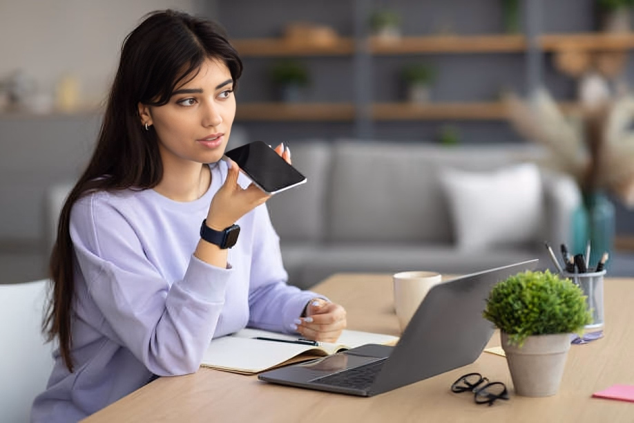 Професійна жінка розмовляє з голосовим помічником під час роботи за офісним столом.