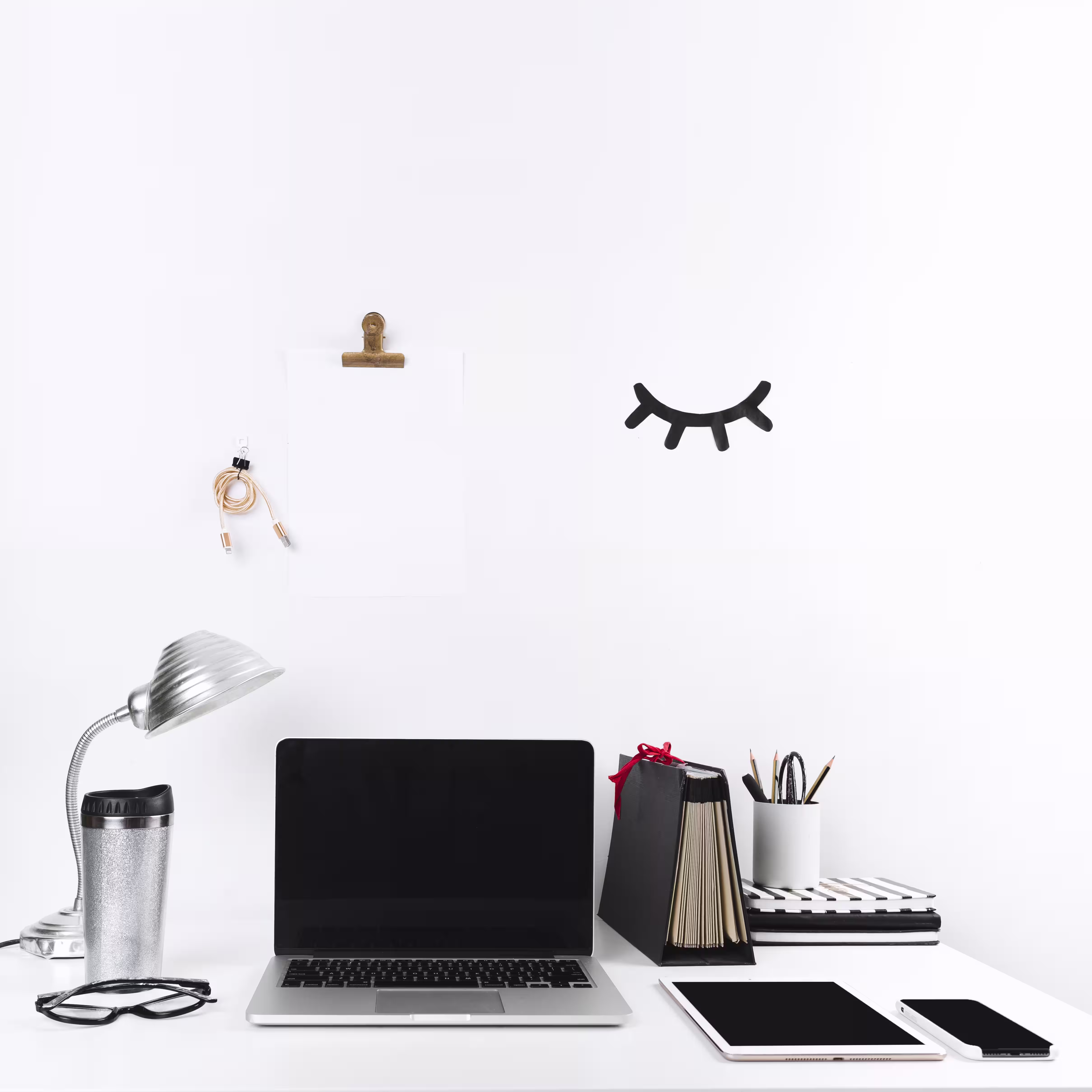 Temiz duvara karşı dizüstü bilgisayar, tablet, telefon ve minimal ofis malzemeleriyle düzenlenmiş beyaz masa